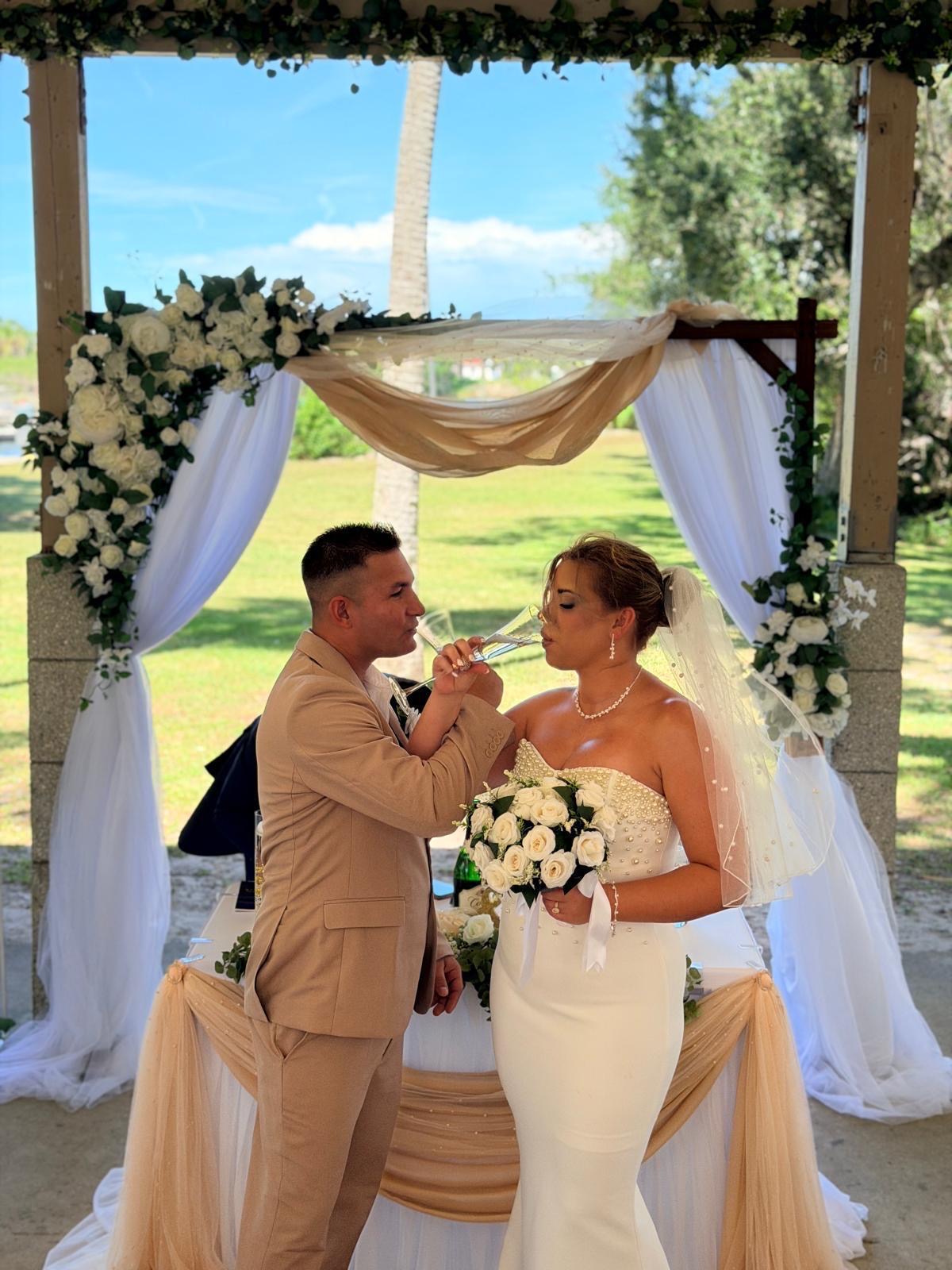 Dianelys and Liyan seated together beneath a champagne draped floral arbor