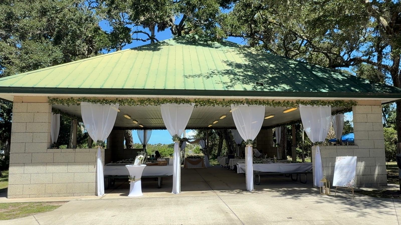 Outdoor pavilion entrance dressed with white fabric and cocktail tables