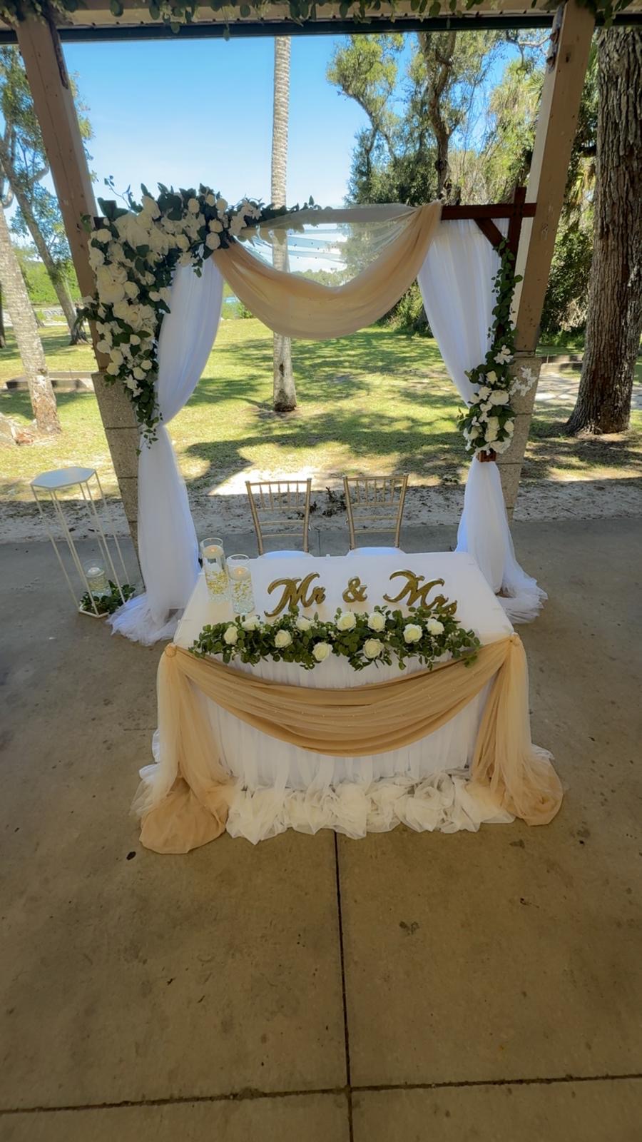 Champagne sweetheart table beneath a floral arbor