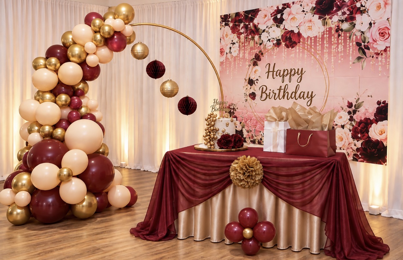 Burgundy, blush, and gold birthday table with balloon arch and floral backdrop